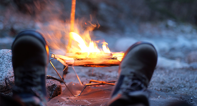 POV of campfire on gravel ground with boots in view