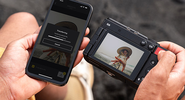 man holding a smartphone and camera transferring content wirelessly